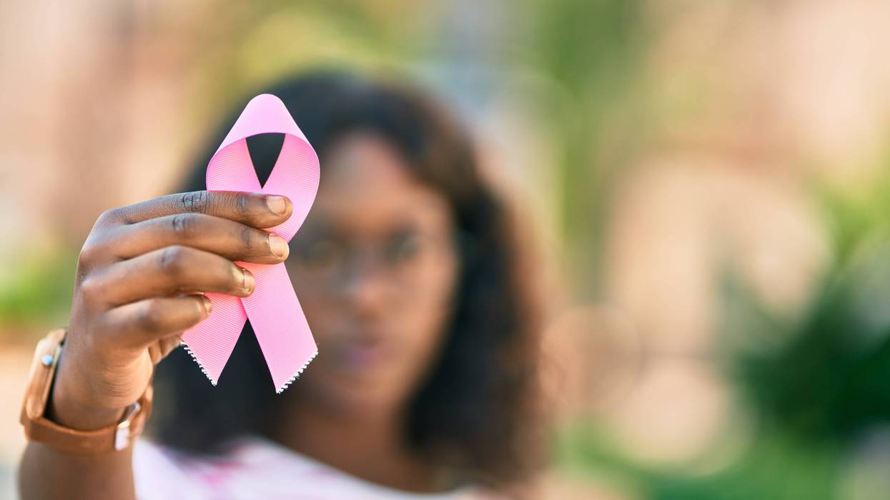 A woman holding a pink ribbon signifying breast cancer.