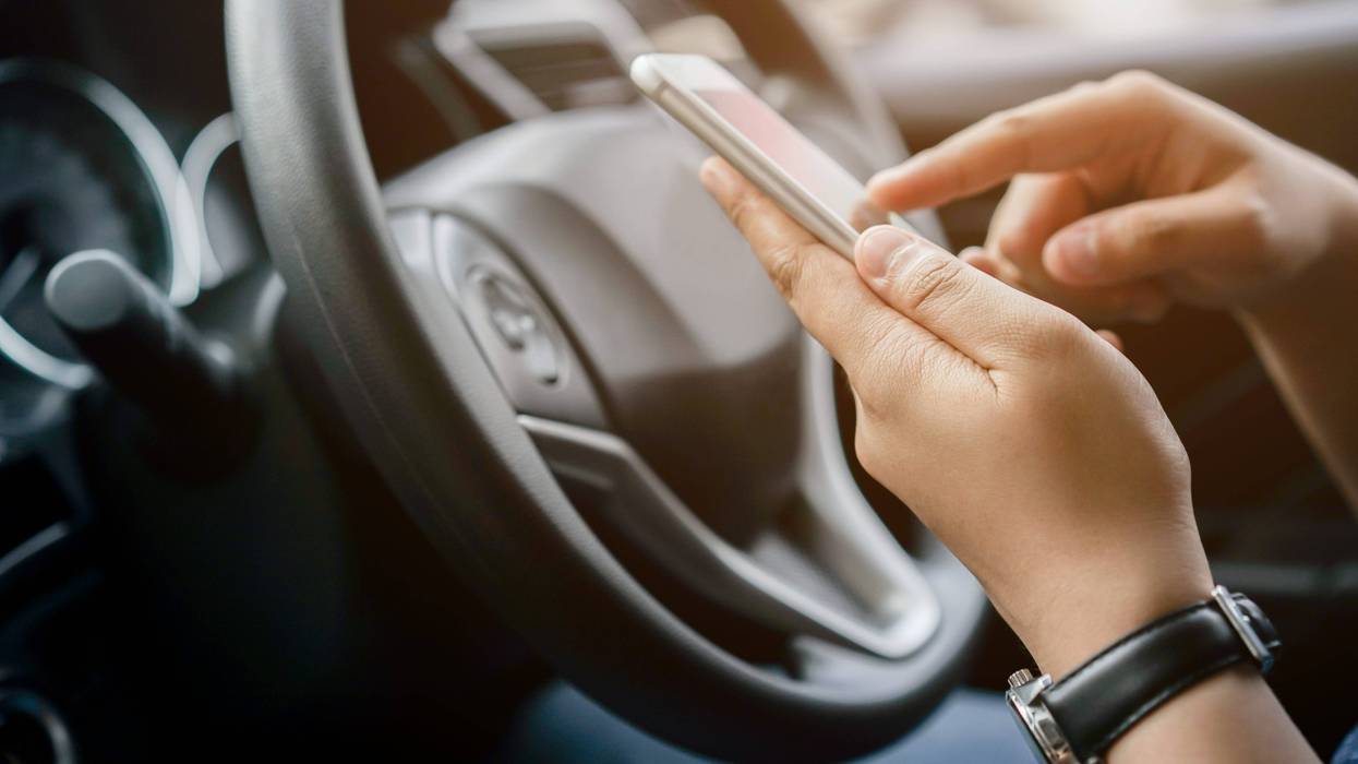 A woman holds a phone while behind the wheel.