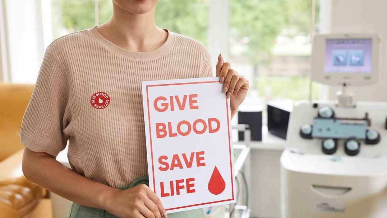 A woman holds a sign that reads "give blood, save a life"