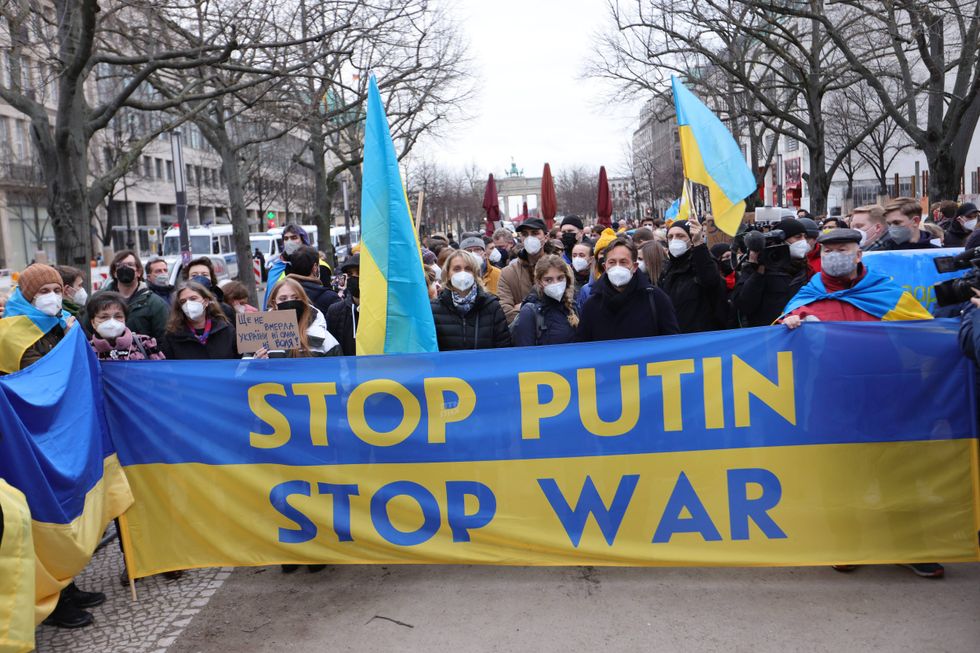 A woman holds a Ukrainian flag next to a banner reading stop Putin as youth groups protest Ukraine intervention with human chain in front of the Russian Embassy on February 22, 2022 in Berlin, Germany