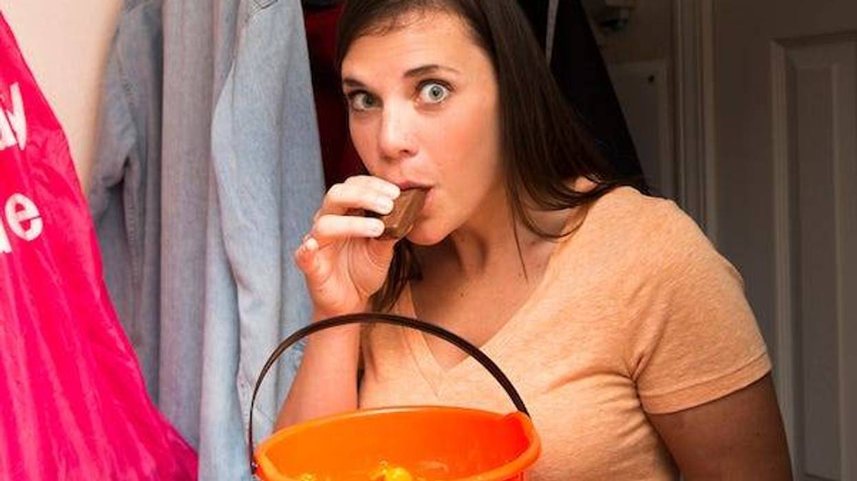 A woman in a dark closet looks startled and guilty when she is caught sneaking the Halloween candy
