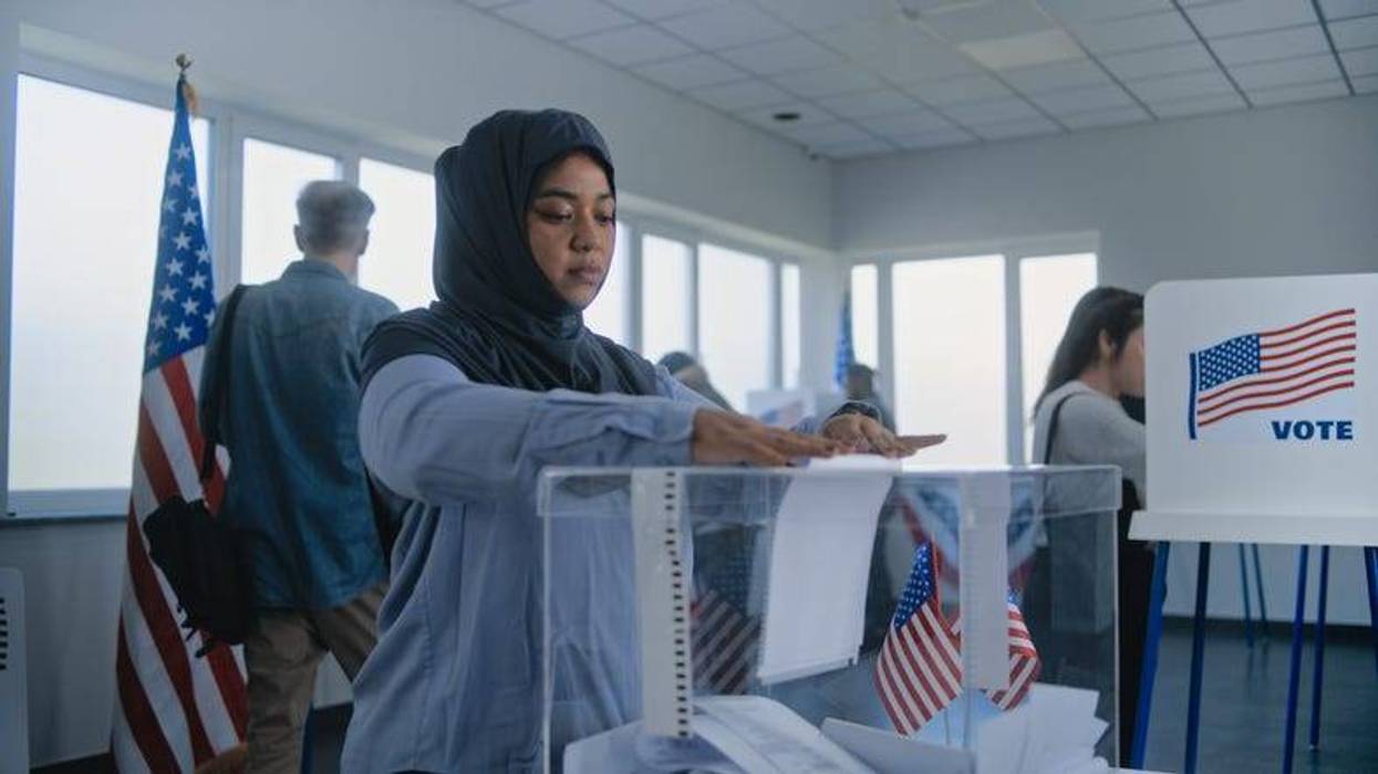 A woman in a hijab drops a ballot into a clear box