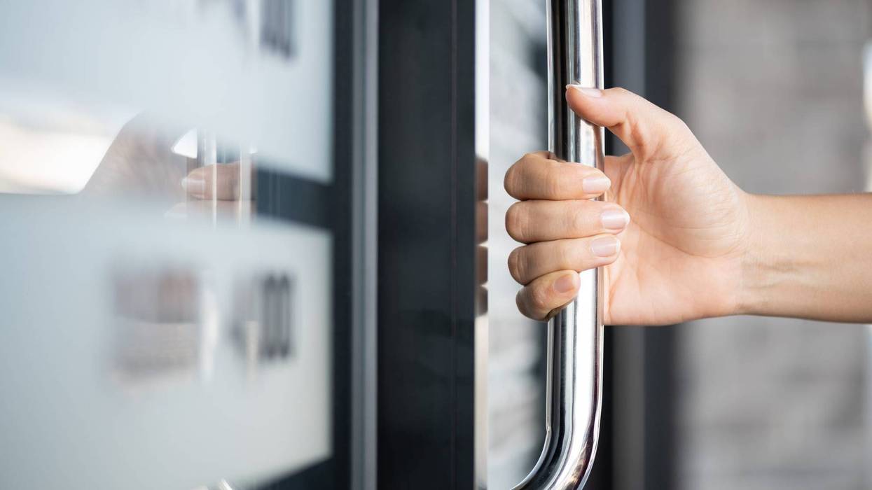 A woman opens a door by pulling a door handle