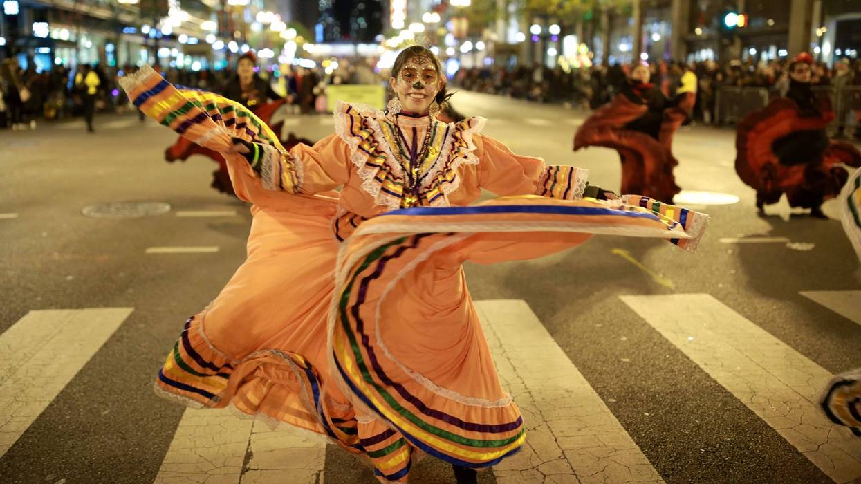 A woman parades and dances in traditional Dia de los Muertos makeup during the Chicago Halloween parade