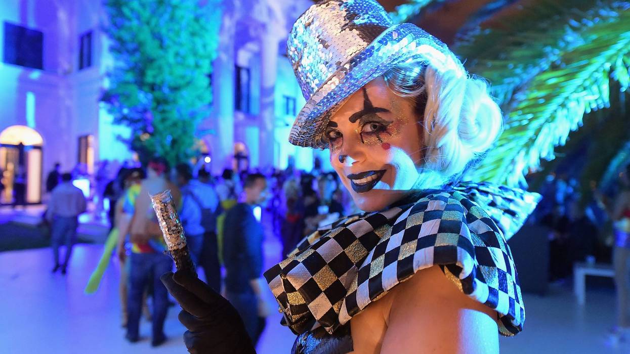 A woman poses in decorative make-up, checkered top and hat in front of a crowd at a Miami Beach party
