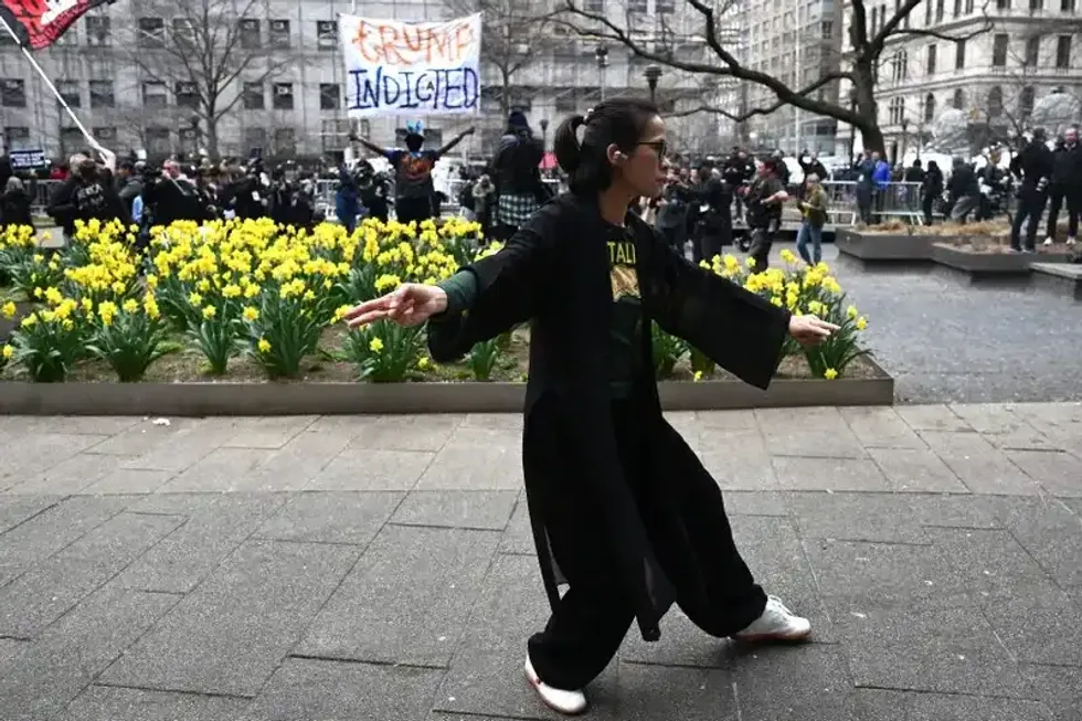 A woman practices tai chi as people protest outside the D.A.