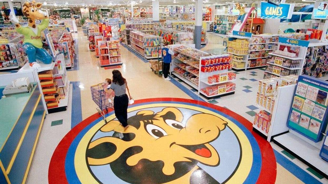 a woman pushes a shopping cart over a graphic of Toys R Us mascot Geoffrey the giraffe at the Toys R Us store