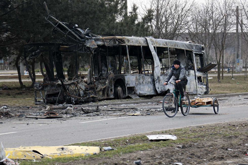 A woman rides a bicycle past a burned bus after fighting on the outskirts of Mariupol, Ukraine, in territory under control of the separatist government of the Donetsk People