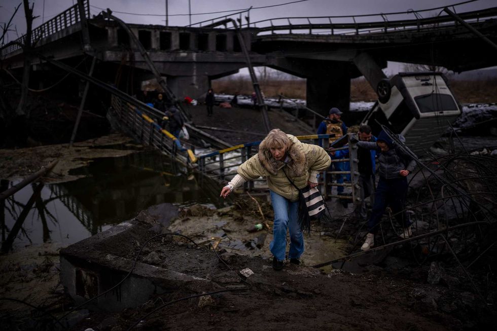 A woman runs as she flees with her family across a destroyed bridge in the outskirts of Kyiv, Ukraine, Wednesday, March 2. 2022