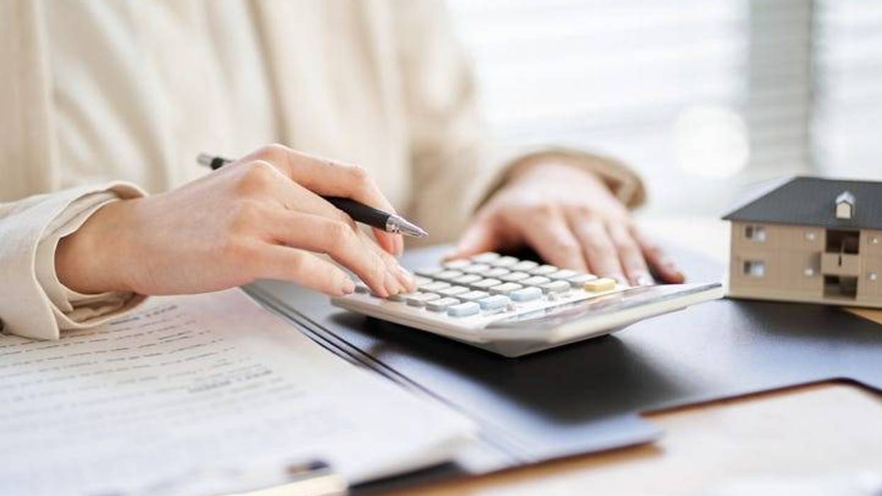 A woman's hands working on a calculator with a small toy model home nearby