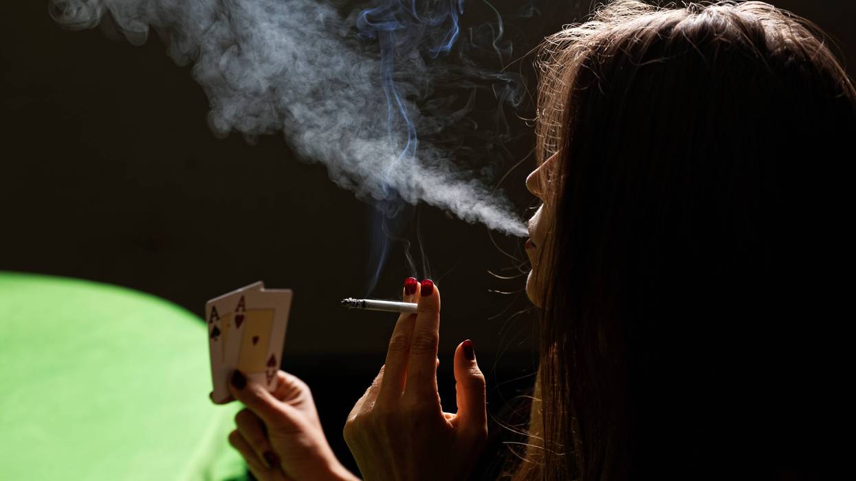 A woman smokes a cigarette while looking at a hand of cards.