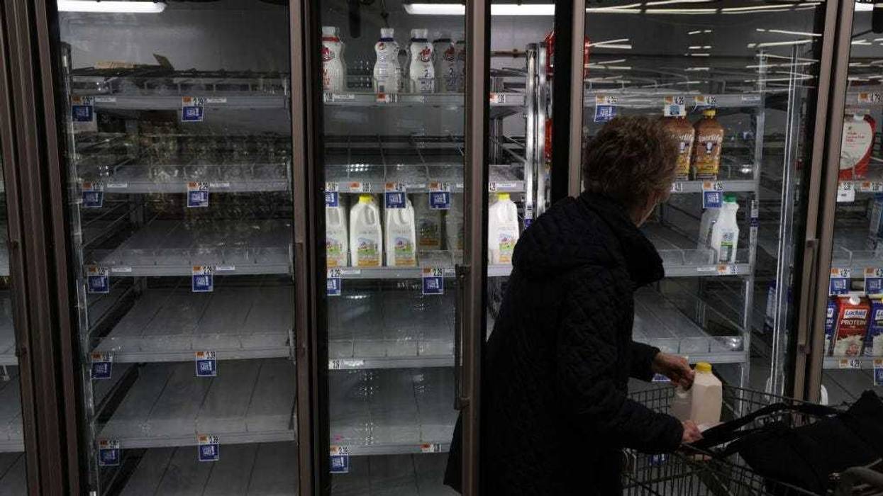 A woman takes a jug of milk off of depleted refrigerated shelves at a Giant Food Supermarket January 12, 2022 in Springfield, Virginia.