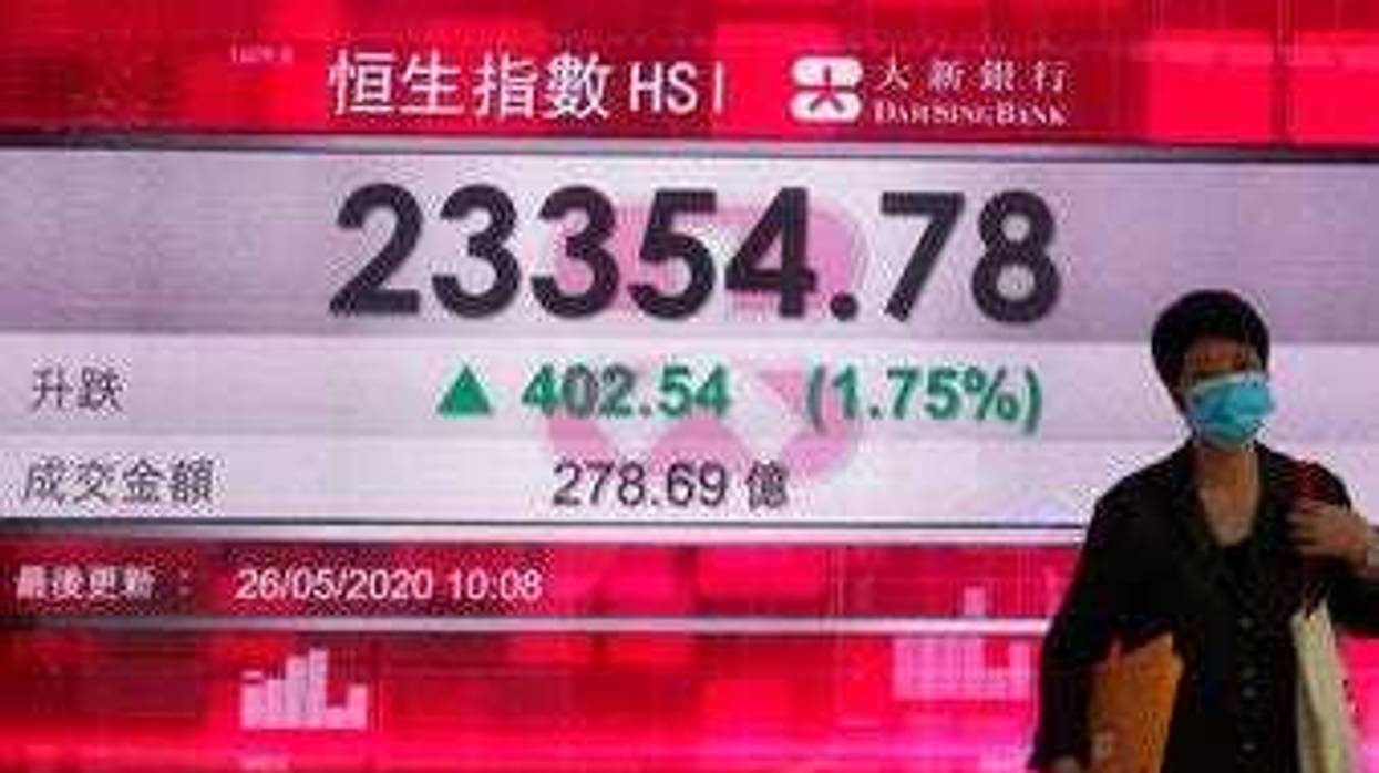 A woman wearing face mask walks past a bank electronic board showing the Hong Kong share index at Hong Kong Stock Exchange Tuesday, May 26, 2020. (AP Photo/Vincent Yu)