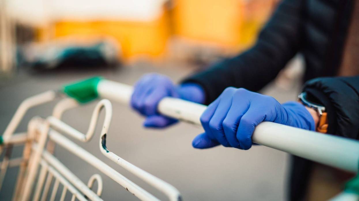 A woman wearing medical gloves grasps the handlebar of a shopping cart