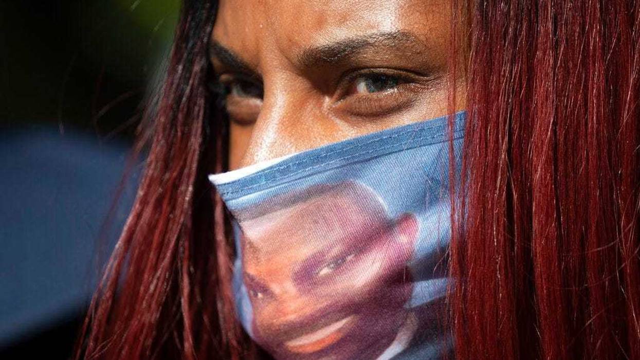 A woman wears a face covering with the likeness of shooting victim Ahmaud Arbery printed on it during a rally to protest Arbery's killing Friday, May 8, 2020, in Brunswick Ga.