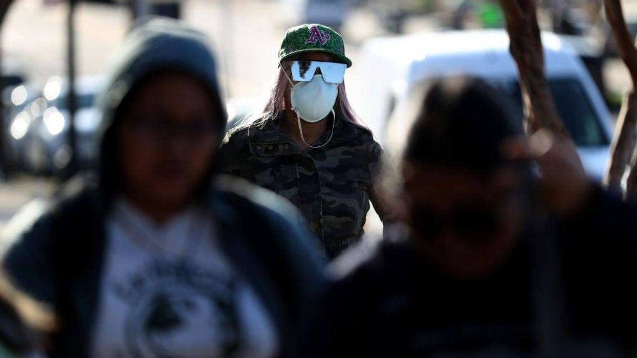 A woman wears a protective mask as she waits in line at Garfield Elementary School to receive a free meal on March 19, 2020 in Oakland, California.
