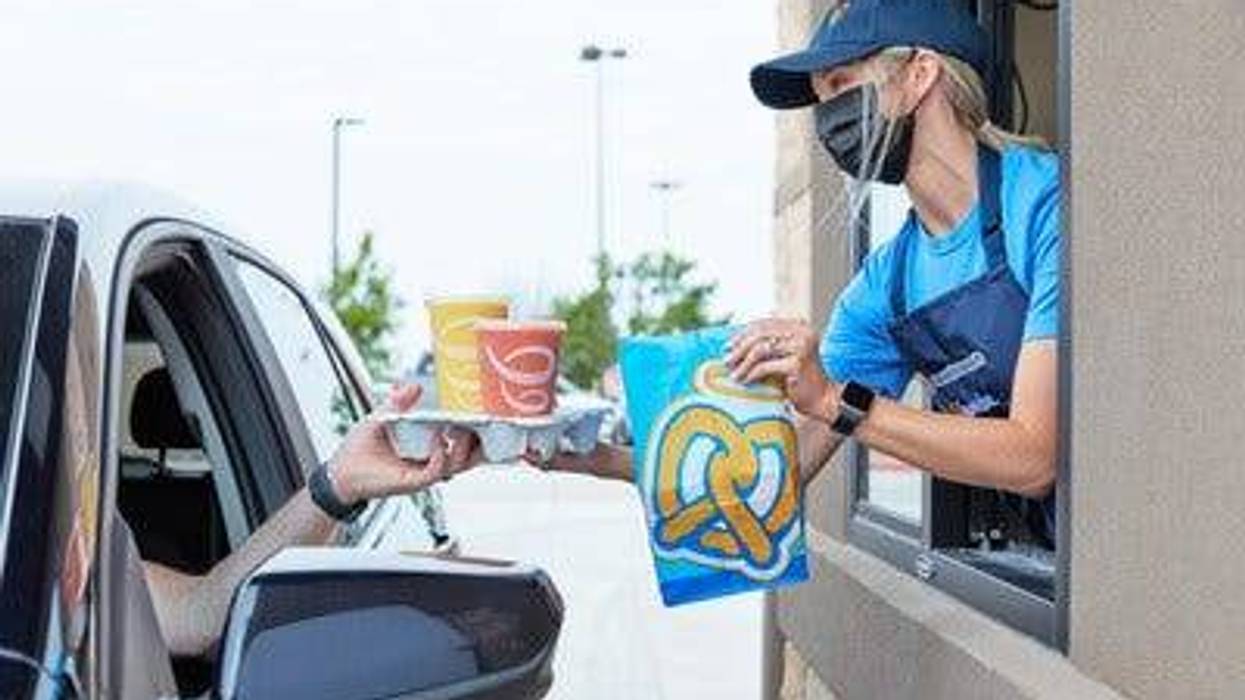 A worker delivering a Auntie Anne's bag and Jamba Juice to a customer via drive-through.