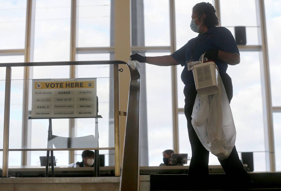 A worker sanitizes a hand rail at a Vote Center located at the Dorothy Chandler Pavilion on the first weekend of early in-person voting on October 25, 2020 in Los Angeles, California.