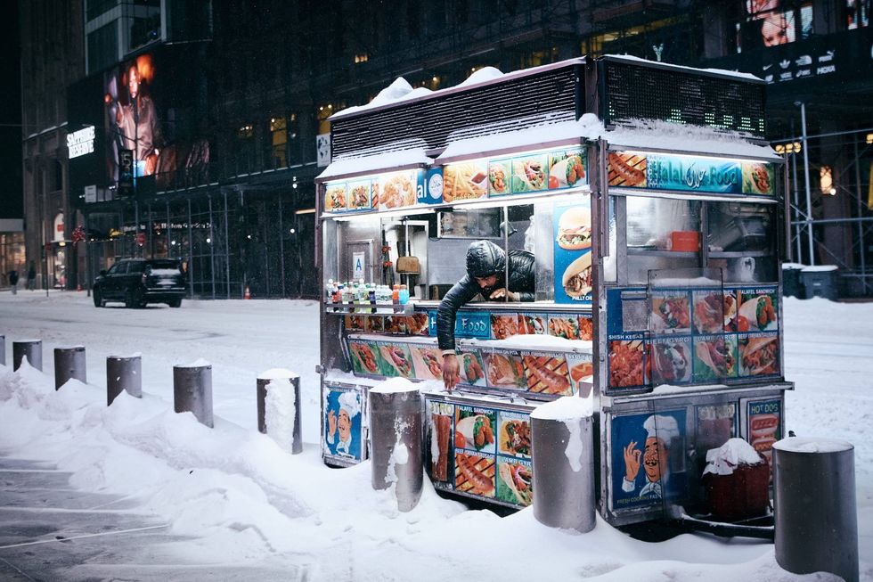 A worker tries to reach a can of soda from his food cart during a snowstorm on Jan. 25, 2026