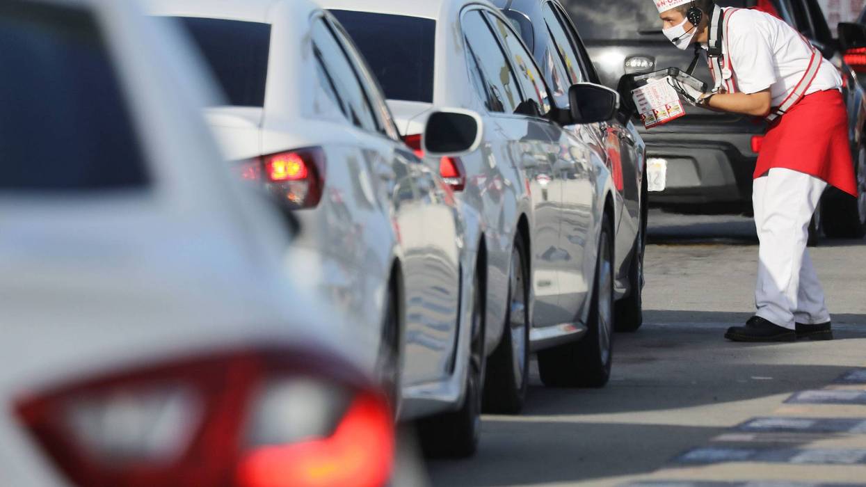 A worker wears a face covering while taking orders from motorists in the drive-through lane at an In-N-Out Burger restaurant amid the COVID-19 pandemic on July 1, 2020 in Los Angeles.