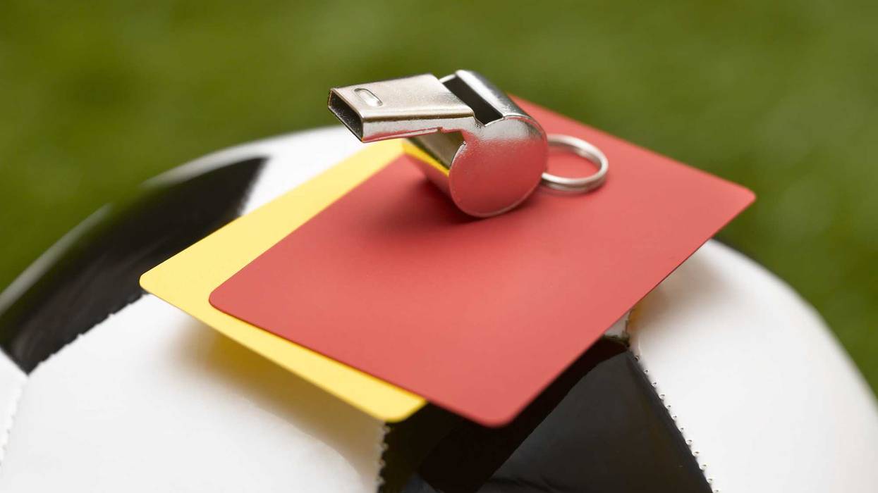 A yellow and red card resting atop a soccer ball with a referee's whistle.