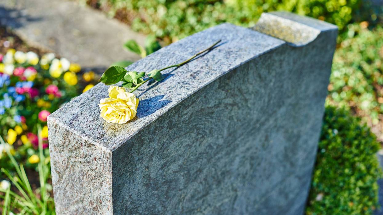 A yellow rose sits atop a gravestone.