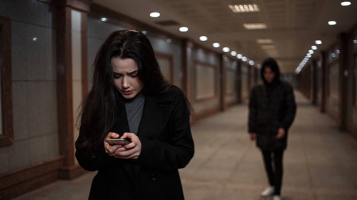 a young beautiful woman walks through an underground passage at night, followed by a man in dark clothing with a hood on his head. a woman tries to dial the number of the rescue service on the phone