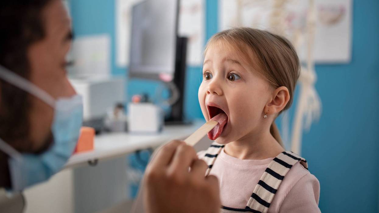 A young male doctor checking little girl's throat in his office.