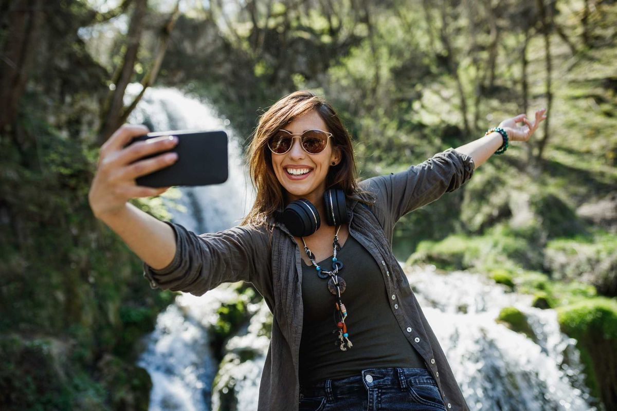 A young woman taking selfie at a waterfall.