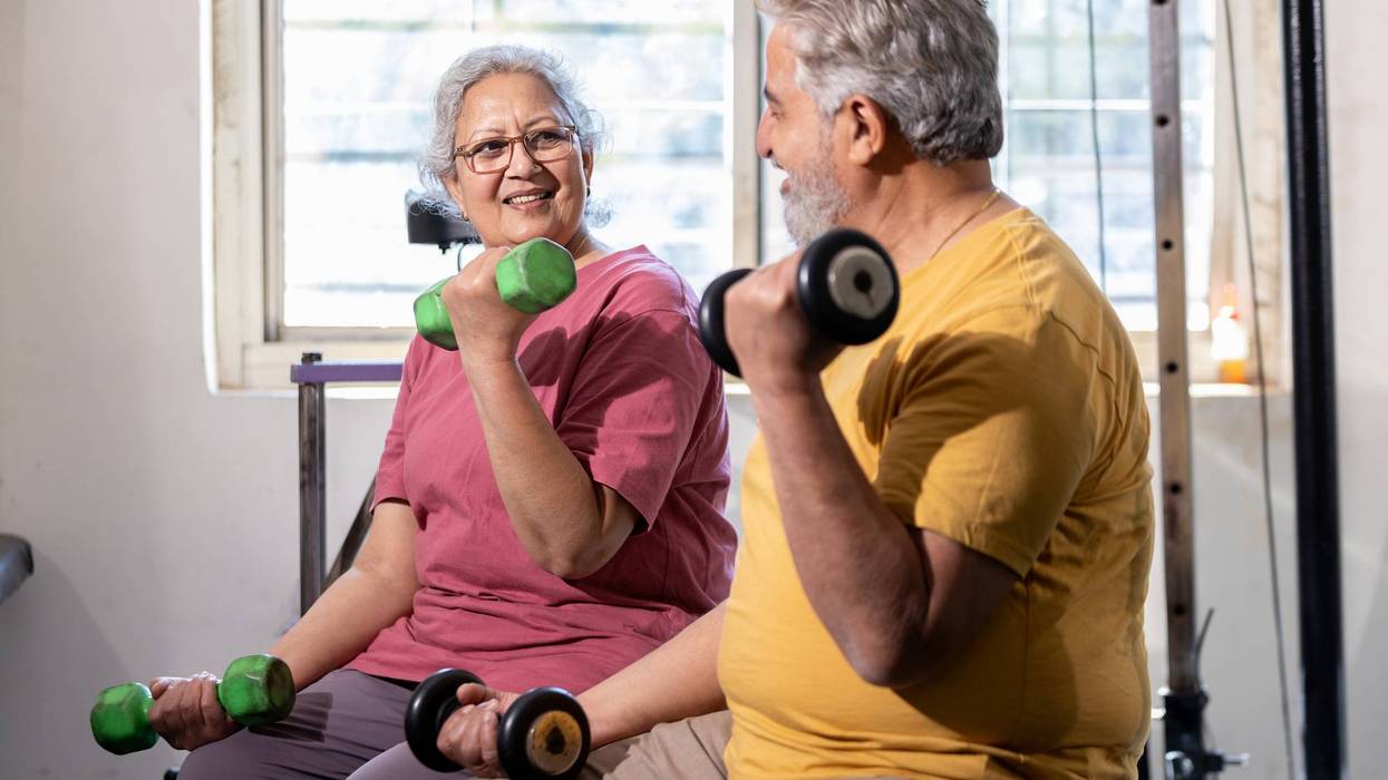 Active indian senior couple doing exercises in gym, Vital elderly people weight lifting training with dumbbells at health club to stay fit.