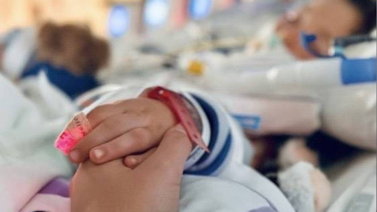 Adult hand holds child's hand with pulse oximeter, hospital band. Blurred hospital background.