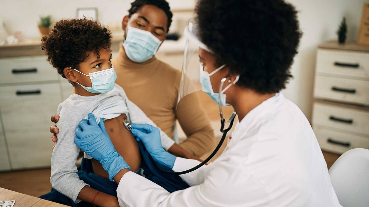 African American boy with face mask being examined by female pediatrician during medical apportionment at doctor's office.