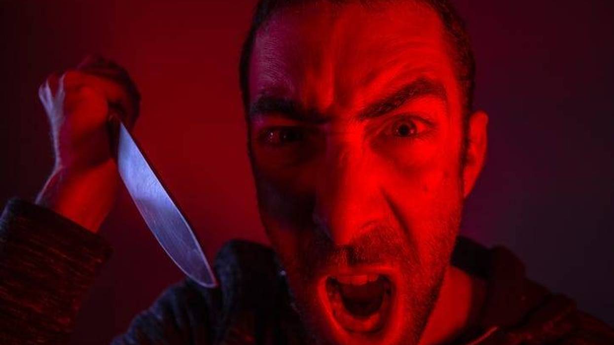 Aggressive man screaming out loud and swinging a knife. Close up portrait of a man with angry facial expression.