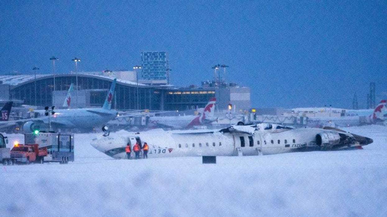 Airport workers survey the site of a Delta Air Lines plane crash that injured at least 18 passengers at Toronto Pearson International Airport on February 18, 2025 in Toronto, Canada. The jet, coming in from Minneapolis, attempted to land amid strong winds and snow, leading to it crashing and landing upside down on the tarmac the day before.