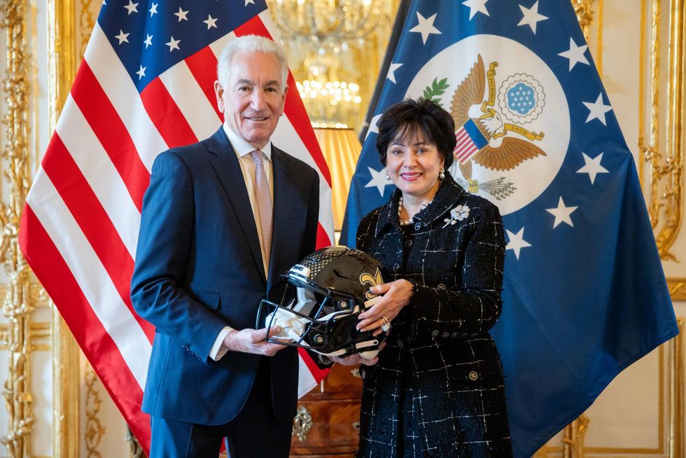 Ambassadors Daniel Fried & Kelly Craft hold a New Orleans Saints helmet, flanked by US flags.