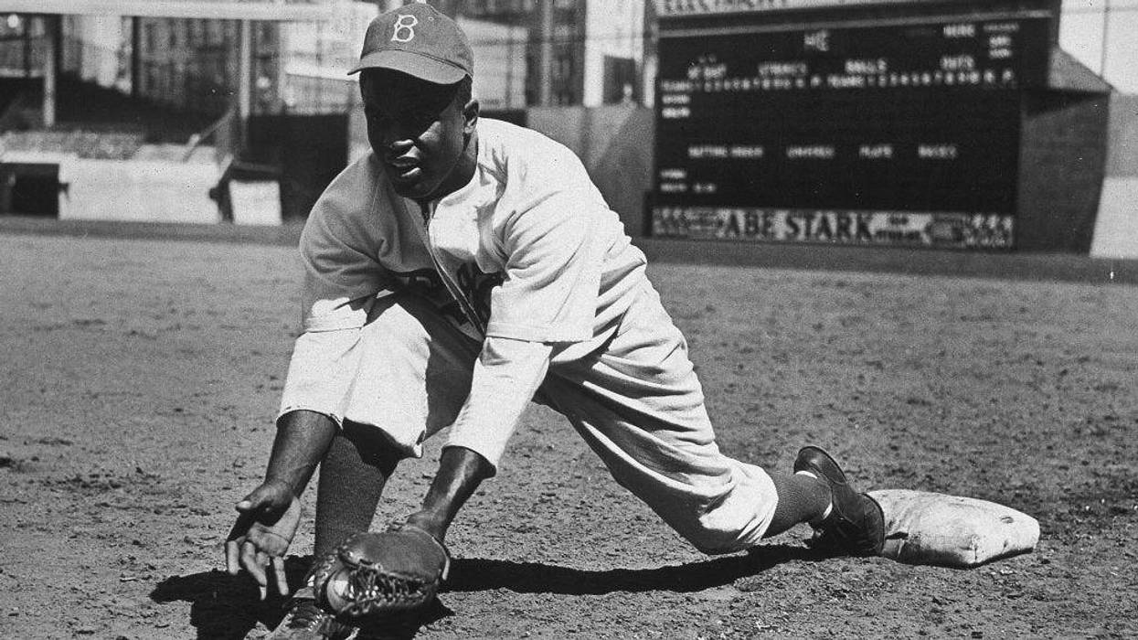 American baseball player Jackie Robinson (1919 - 1972) grounds a ball at first place while warming up for an exhibition game against the New York Yankees, Ebbets Field, NYC, 1950s.
