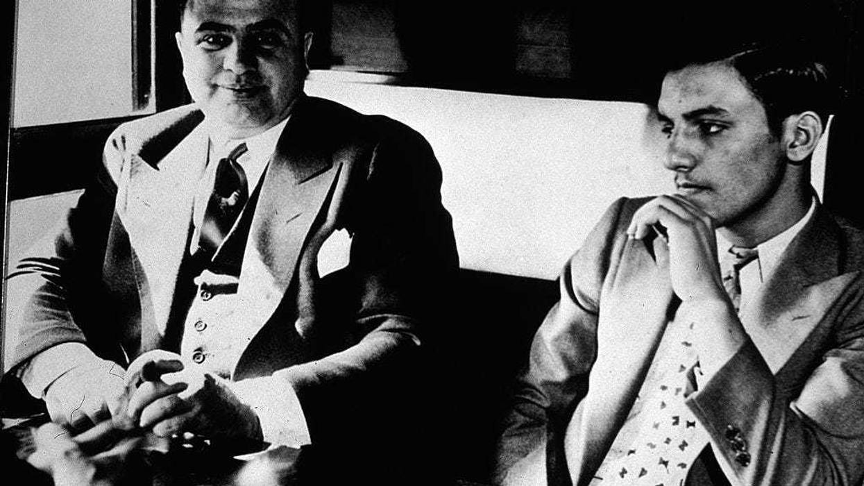 American gangster Al Capone ('Scarface') (1899 - 1947) sits in a train compartment with an unidentifed associate (R) during his transport to prison to serve a sentance for tax evasion, October 1931. (Photo by Hulton Archive/Getty Images)