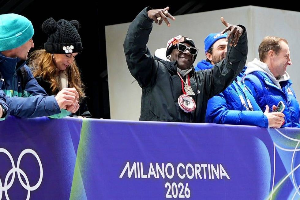 American rapper Flavor Flav, center, attends the skeleton mixed team competition at the 2026 Winter Olympics, in Cortina d