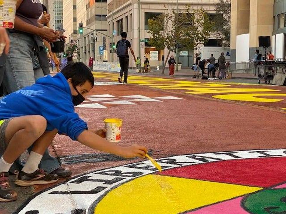 An activist paints a colorful "Choose Democracy" mural Thursday afternoon in downtown Oakland.
