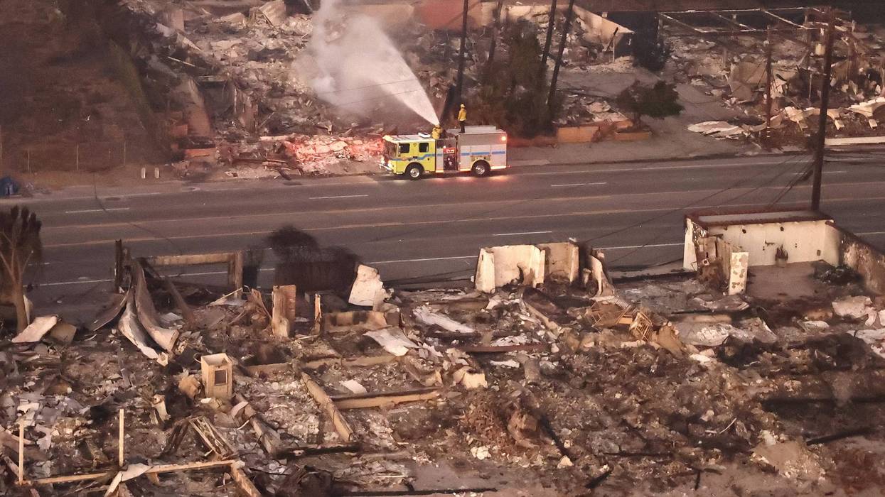 An aerial view of firefighters spraying water on a destroyed property as the Palisades Fire continues to burn on January 09, 2025 in Malibu, California.