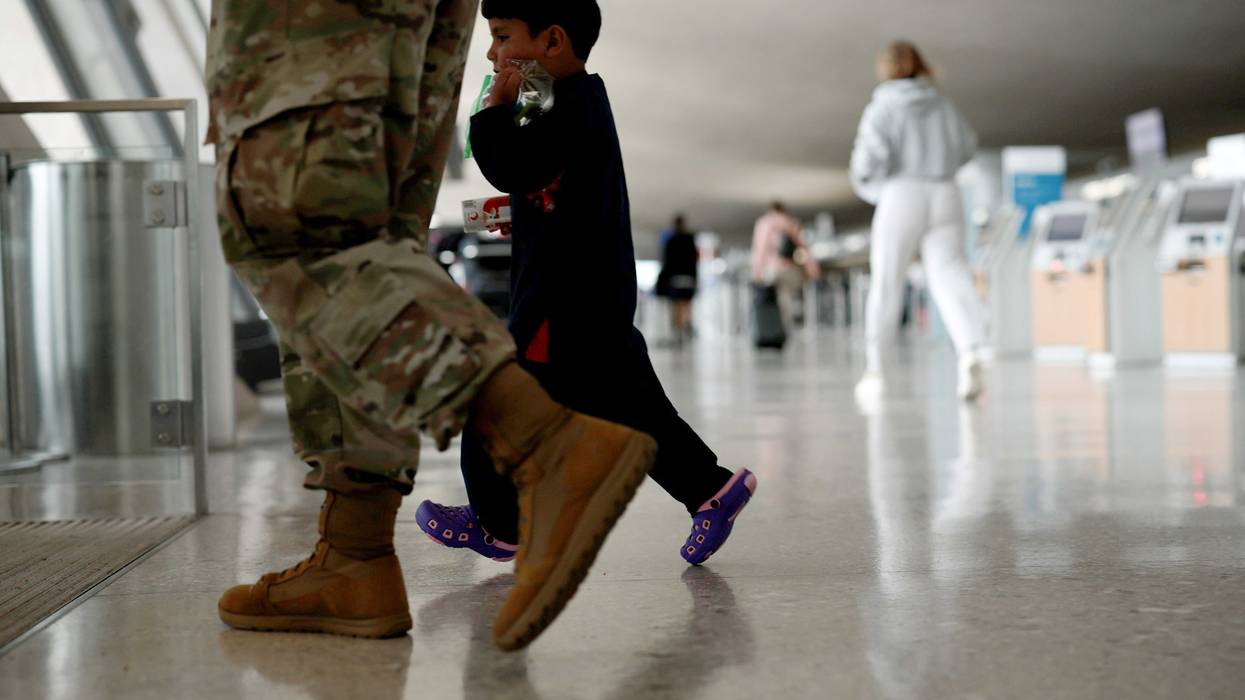 An Afghan boy walks with a U.S. service member as he and his family are led through the Dulles International Airport to board a bus that will take them to a refugee processing center after being evacuated from Kabul following the Taliban takeover of Afghanistan on August 31, 2021 in Dulles, Virginia.