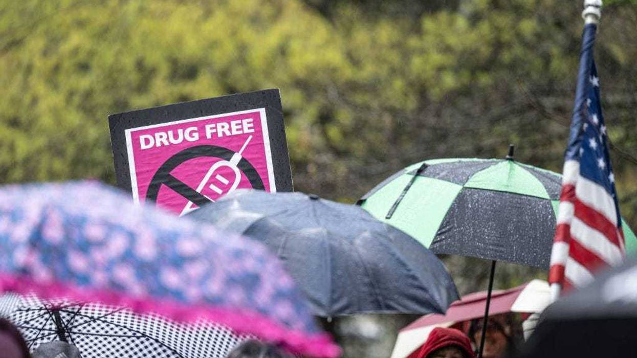 An anti-vaccination sign is seen above a row of umbrellas while demonstrators chant with speakers during a protest on state capitol grounds on April 14, 2021 in Frankfort, Kentucky. (Photo by Jon Cherry/Getty Images)