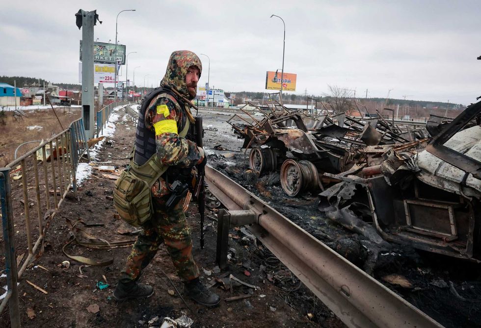 An armed man stands by the remains of a Russian military vehicle in Bucha, close to the capital Kyiv, Ukraine, Tuesday, March 1, 2022