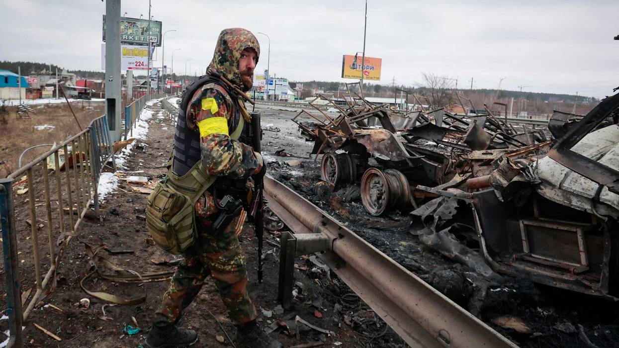 An armed man stands by the remains of a Russian military vehicle in Bucha, close to the capital Kyiv, Ukraine, Tuesday, March 1, 2022
