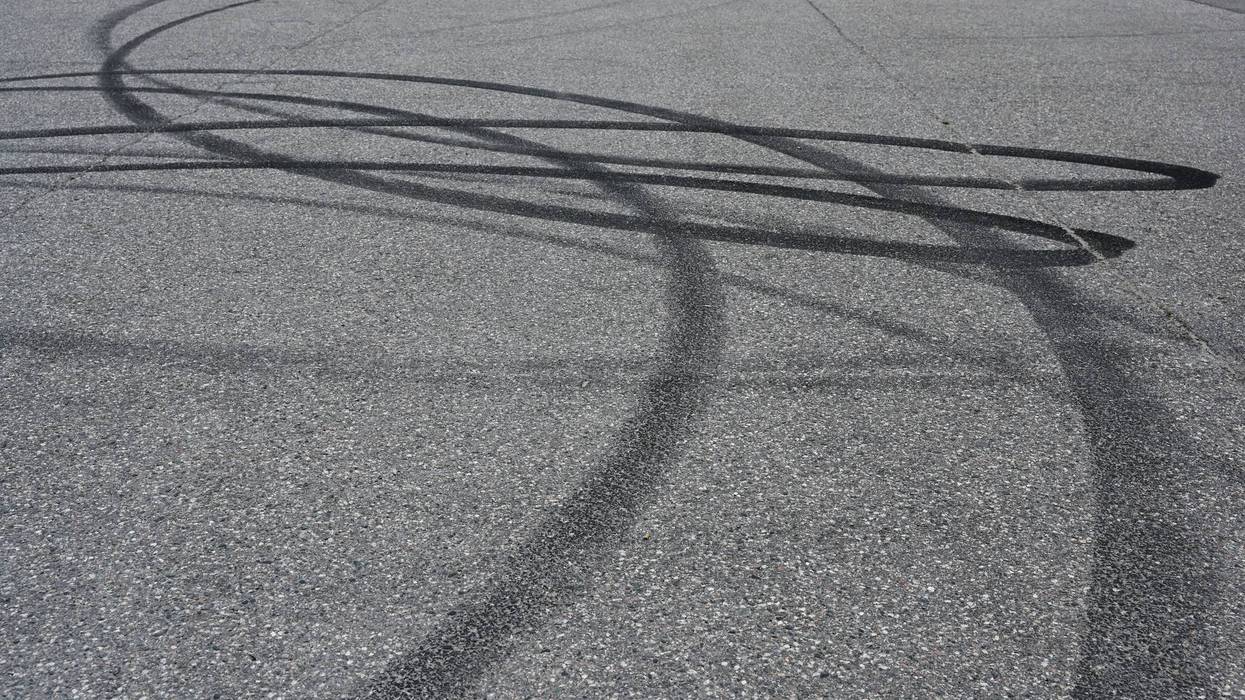 an asphalt surface covered in overlapping tire skid marks from high-speed driving maneuvers such as drifting or burnouts