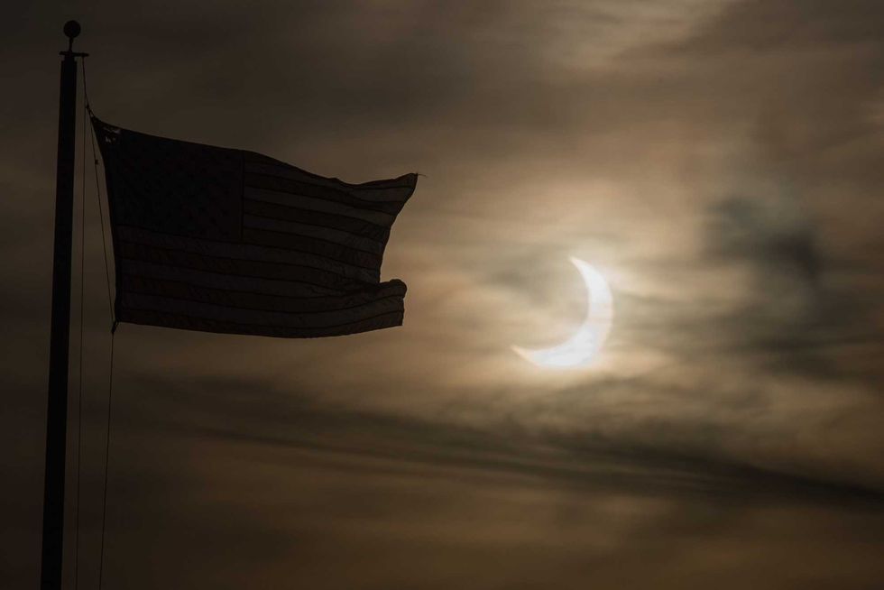 An eclipsed sun rises next to a flag on June 10, 2021 in Scituate, Massachusetts. Northeast states in the U.S. will see a rare eclipsed sunrise, while in other parts of the Northern Hemisphere, this annular eclipse will be seen as a visible thin outer ring of the sun
