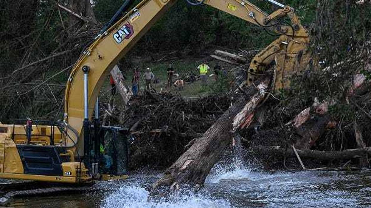 an excavator removes trees damaged in the Central Texas floods along the Guadalupe River as they search for victims on July 9, 2025 in Center point, Texas. Over a 100 people have died in the Central Texas floods and over 160 people remain missing