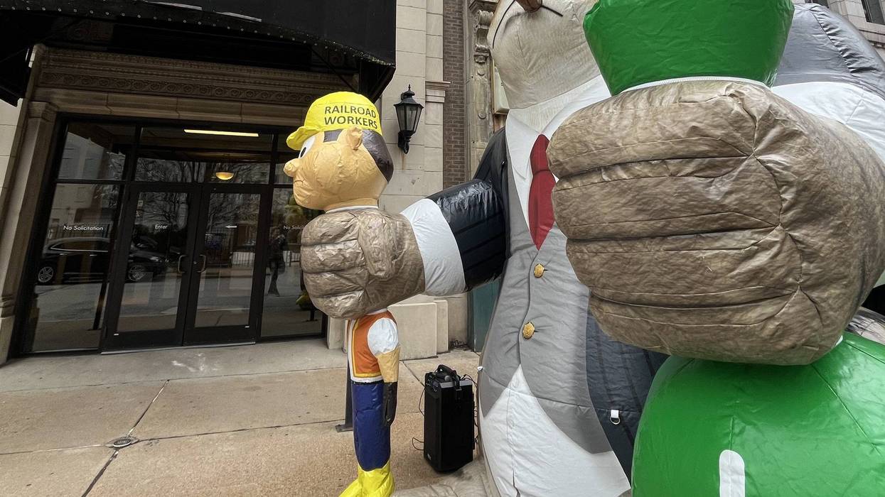 An inflatable fat cat, holding a bag of money and a railroad worker.