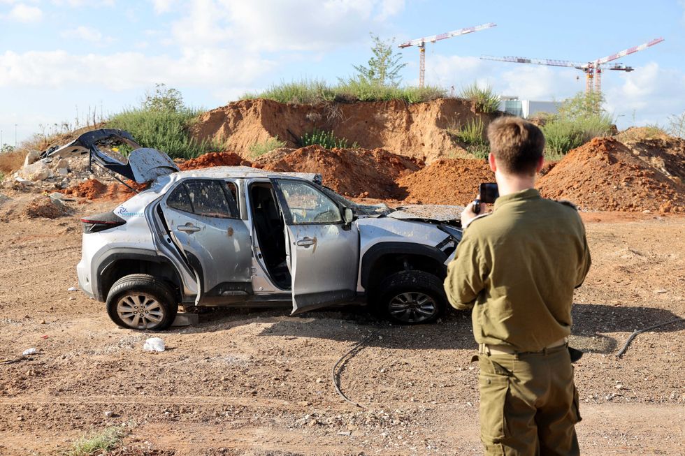 An Israeli soldier takes a picture of a damaged vehicle in the aftermath of an Iranian missile attack in Tel Aviv on October 2, 2024