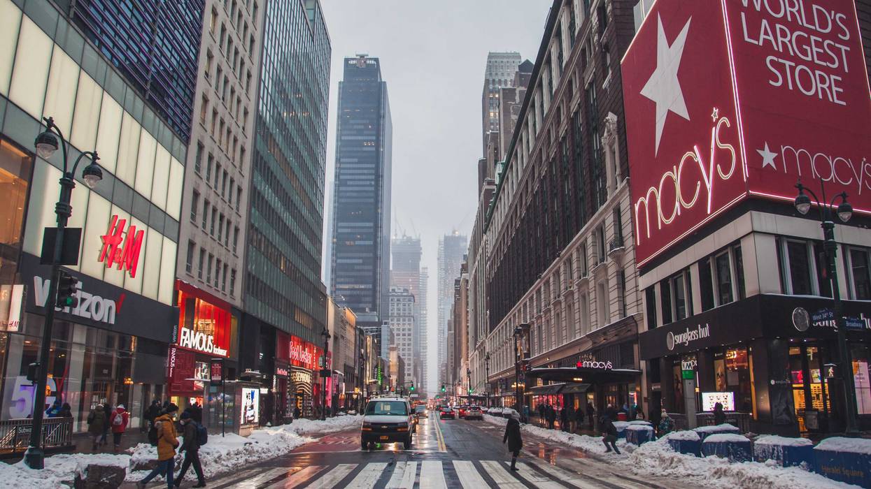 An NYC midtown street. Tourists cross the iconic intersection of 34th Street & 6th Ave carefully choosing their path because the street is covered with snow.